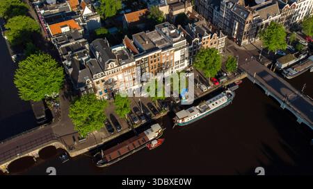 Vue aérienne des péniches amarrées le long du canal, reflétant la lumière chaude contre l'eau sombre, près du pont et des bâtiments, Amsterdam, North Hô Banque D'Images