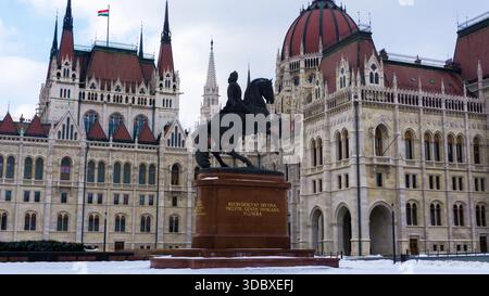 Vue d'une statue équestre majestueuse se dresse fièrement devant le bâtiment orné du Parlement hongrois, coiffé d'un dôme rouge, dans le paysage enneigé, B. Banque D'Images