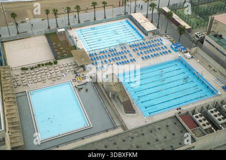 Vue sur les piscines turquoise scintillent sous le soleil près d'une plage de sable, tandis que les palmiers balancent doucement dans la brise, Barcelone, Catalogne, Espagne. Banque D'Images