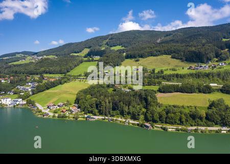 Vue aérienne du lac émeraude reflétant les collines verdoyantes parsemées de maisons sous un ciel bleu vif, Mondsee, haute-Autriche, Autriche. Banque D'Images