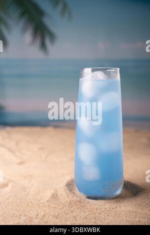 boisson bleue fraîche dans un grand verre serrée sur une plage de sable avec des frondes de palmiers et un horizon océanique, évoquant des vibrations tropicales sereines et une détente estivale rafraîchissante Banque D'Images