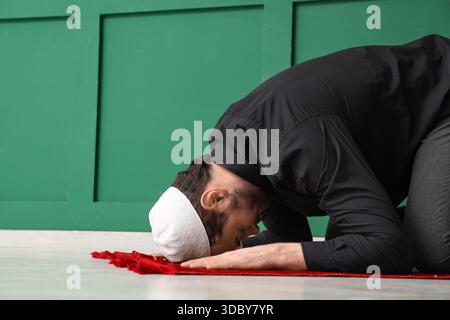 Jeune homme musulman priant sur le tapis de prière à la maison. Célébration du Ramadan Banque D'Images
