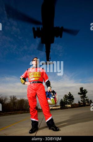 Concord, Caroline du Nord, 21 décembre 2006 : le pilote NASCAR Greg Biffle pose lors de sa séance photo de pré-saison avec la Garde nationale alors qu'un hélicoptère Apache de l'armée monte au-dessus du ciel, fusionnant course et précision militaire. Banque D'Images