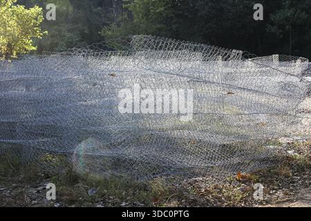 Rouleau de clôture en treillis métallique d'acier galvanisé industriel posé sur le sol à l'extérieur dans la nature avec des motifs de texture métallique évoquant la sécurité robuste et la constr Banque D'Images
