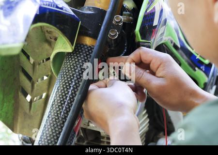 Mains de mécanicien focalisées réparant le système de fil sur le véhicule de motocross avec une attention particulière montrant la concentration pendant la session de maintenance en extérieur avec Banque D'Images
