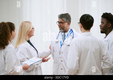 Groupe multiethnique de médecins d'âge moyen et de jeunes adultes discutant des soins aux patients Banque D'Images