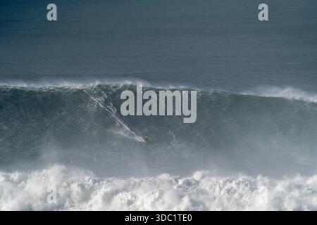 Surfeuse face à une puissante vague à Praia do Norte, Nazaré, Portugal. Emplacement emblématique de l'océan Atlantique pour le surf extrême des femmes. Banque D'Images