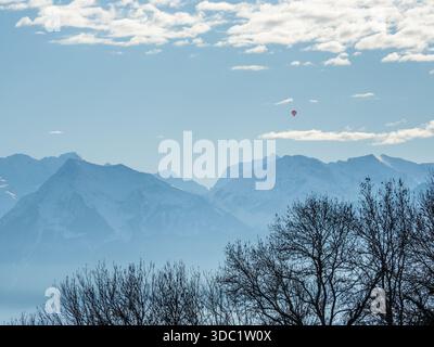 Montgolfière au-dessus des Alpes suisses enneigées avec des arbres silhouettes Banque D'Images