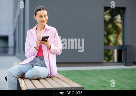 Femme utilisant smartphone sur le banc extérieur Banque D'Images