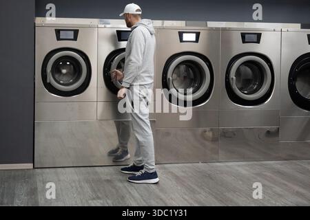 Homme utilisant le lave-linge libre-service dans la laverie moderne Banque D'Images