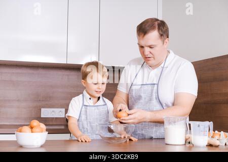 Papa et fils dans la cuisine, père apprend à l'enfant à casser des œufs dans un bol. Cuisiner ensemble à la maison. Le fils aide ses parents. Joyeuse fête des pères || autorisation du modèle Banque D'Images