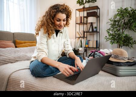 Jeune femme planifiant un voyage de voyage et emballant une valise sur le lit Banque D'Images