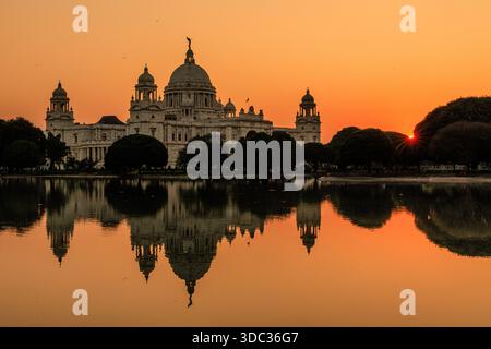 mémorial kolkata victoria et ciel orange brillant reflété dans le lac placide avec le coucher du soleil derrière les arbres environnants Banque D'Images