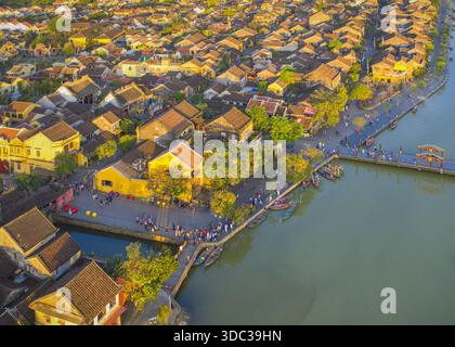 Vue aérienne de la lumière dorée baignant les toits en terre cuite de l'ancienne ville et le bord de rivière animé, Hoi an, Quang Nam, Vietnam. Banque D'Images