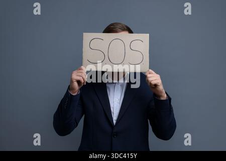 Homme tenant l'affiche en carton avec SOS sur fond gris Banque D'Images