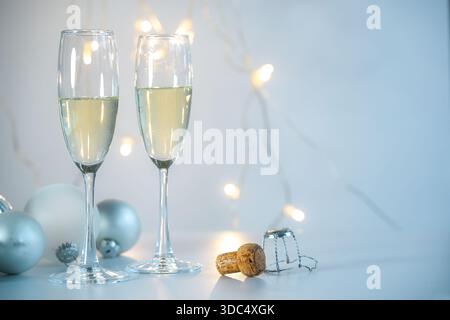 Deux flûtes à champagne, boules de Noël argentées et le liège sur un fond bleu clair avec quelques lumières de fées, fête festive sur un jour férié comme Banque D'Images