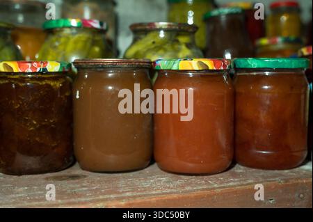 Des bocaux de diverses conserves de fruits faites maison et des légumes marinés sont stockés sur une étagère rustique dans un garde-manger sombre, mettant en valeur le stockage traditionnel des aliments et Banque D'Images