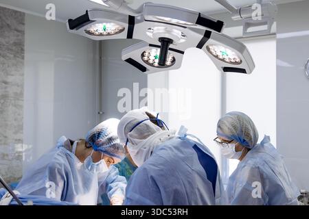 L'équipe chirurgicale dans les gommages bleus est engagée dans une procédure sous des lumières vives, mettant l'accent sur la collaboration et la compétence dans un setti médical propre et professionnel Banque D'Images