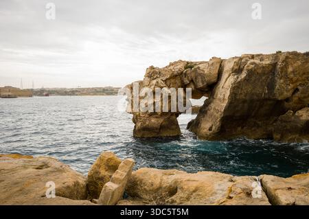 Formation rocheuse côtière avec une arche naturelle, mettant en valeur la beauté de l'érosion. Les eaux turquoises de la mer contrastent avec la roche dorée. Un vi pittoresque Banque D'Images