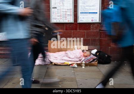 Personne sans-abri non reconnue couchée sur un tapis de carton recouvert d'une couverture sur le trottoir dans les rues de Londres. Banque D'Images