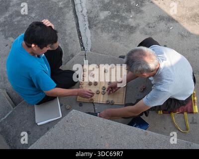 Beijing-Beijing-Chine-18 août 2018,deux hommes jouent un jeu traditionnel de xiangqi (échecs chinois) en plein air sur un trottoir en béton dans un cadre urbain. Banque D'Images