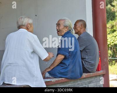 beijing-Beijing-Chine-21 août 2018,trois hommes asiatiques seniors assis sur un rebord parlant et souriant dans un cadre de parc. L'homme dans la chemise bleue est animat Banque D'Images