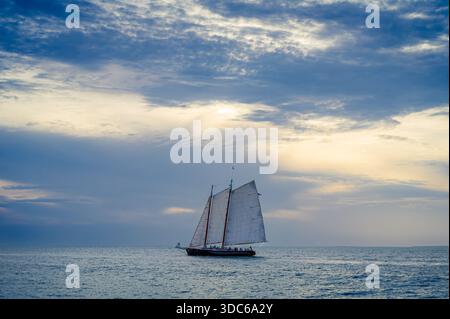 Voilier solitaire naviguant dans l'horizon à Key West, lumière de fin d'après-midi sur une journée nuageuse, Floride Banque D'Images