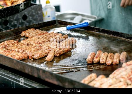 Kebabs de viande cevapcici grillés frais cuisant sur une plaque chauffante. Saucisses de viande hachée traditionnelles des Balkans préparées pour servir au festiva de la nourriture en plein air Banque D'Images