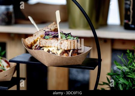 Délicieux sandwich artisanal avec fromage fondu de chou violet microgreens dans un plateau en papier artisanal sur un présentoir noir. Restaurant élégant servant du café Banque D'Images