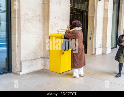 Paris, France - 29 octobre 2025 : LA POSTE boîte aux lettres française Paris logo jaune bureau de poste. Femme envoie du courrier jette une lettre et un colis dans la boîte aux lettres. Enseigne postale France Street. Banque D'Images