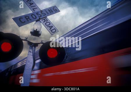 Les signaux de passage à niveau sont activés par des feux rouges lorsqu'un train traverse le passage à niveau. Le ciel est rempli de nuages, créant un sce spectaculaire Banque D'Images