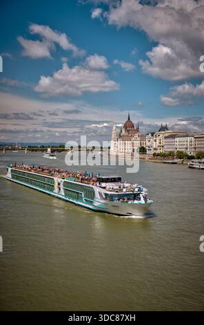 Un bateau de croisière navigue le long du Danube devant le bâtiment du Parlement hongrois dans le centre de Budapest Banque D'Images