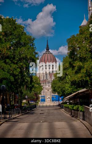 Une vue sur le dôme arrière du bâtiment du Parlement hongrois encadré par des arbres luxuriants le long d'une rue calme dans le centre de Budapest par une claire journée d'été. Banque D'Images