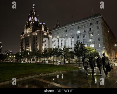 La statue des Beatles à Pier Head, Liverpool — des personnages en bronze éclairés sous l'architecture emblématique du front de mer par une nuit claire Banque D'Images