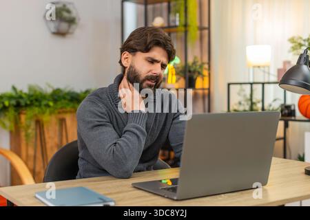 L'homme indien à la maison travaille sur ordinateur portable se sent mal au cou frotte les sourcils du cou arrête la tâche pour se reposer ferme le couvercle. Arabian Guy à la réception massages cou souffle lent humeur malheureuse a besoin de pause après effort de longue session Banque D'Images