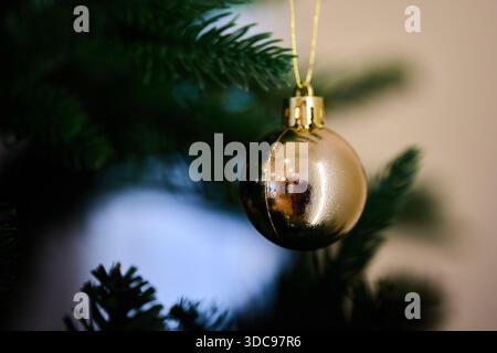 La décoration de boule dorée est accrochée à une branche de sapin de Noël vert. Banque D'Images