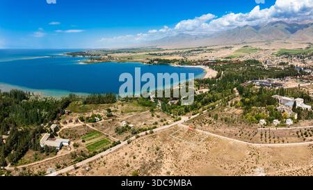 Vue de paysage aérien serein avec montagnes, eau, et station balnéaire dans le lac Issyk-Kul près de Cholpon-Ata, Kirghizistan Banque D'Images