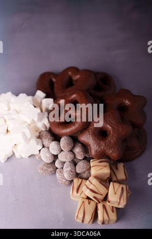 assortiment de bretzels recouverts de chocolat, de guimauves blanches, d'amandes saupoudrées de cacao et de caramel mouillé sur une surface grise mate avec une lumière douce Banque D'Images