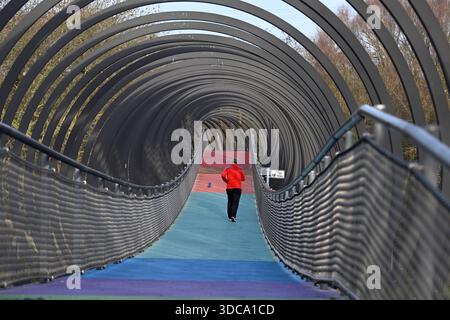 Oberhausen, Allemagne. 21 décembre 2025. Un jogger traverse le pont « Slinky Springs to Fame » sur le canal Rhin-Herne dans le Kaisergarten par des températures agréables qui sont trop élevées pour la période de l'année. Les météorologues prédisent des températures plus basses pour la semaine de Noël, mais avec beaucoup de soleil. Crédit : Roberto Pfeil/dpa/Alamy Live News Banque D'Images