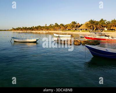 Scène matinale tranquille sur la magnifique plage de sable d'Akumal, Mexique. Les bateaux de pêche reposent dans la baie tandis que le calme des Caraïbes reflète la douce lumière précoce. Banque D'Images