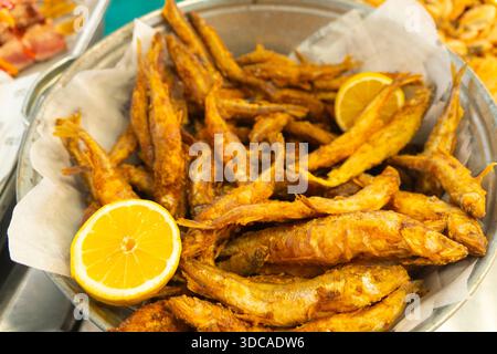 Délicieux petit poisson frit doré croustillant garni de moitiés de citron jaune frais dans un récipient en métal avec du papier blanc Banque D'Images