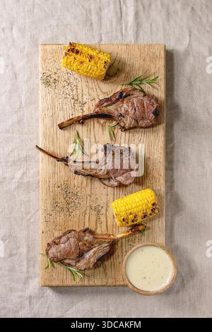 Carré d'agneau grillé au barbecue avec des épis de maïs sucré, de romarin et de la sauce au fromage sur la planche à découper en bois sur toile de fond. Mise à plat, de l'espace Banque D'Images