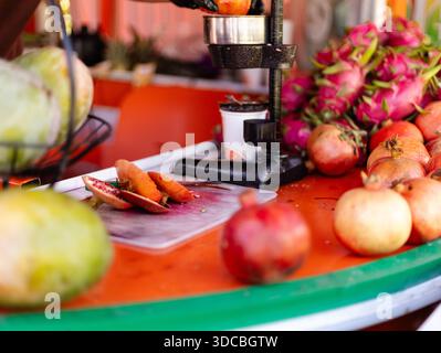 Les jus sont préparés sur un stand de marché avec divers fruits exposés. Les grenades et les fruits du dragon reposent sur le comptoir. L'heure semble être l Banque D'Images