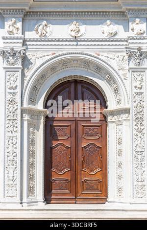 Une grande entrée historique avec une arche en pierre richement sculptée, des reliefs décoratifs et une double porte en bois sombre. Parfait pour l'architecture, le patrimoine, Banque D'Images