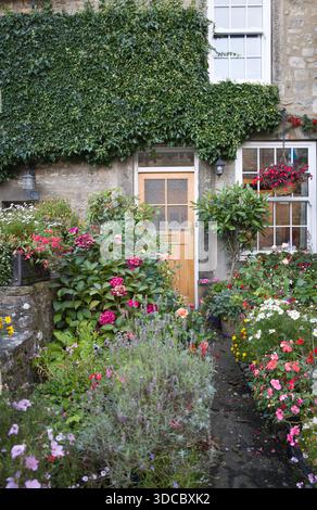 Porte d'entrée à un chalet anglais pittoresque à Grassington Royaume-Uni, avec jardin avant étroit plein de fleurs, murs couverts de lierre, et un chemin de jardin accueillant Banque D'Images