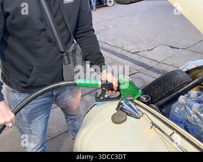 Homme faisant le plein d'une voiture Volkswagen classique par l'arrière à l'aide d'une pompe à essence verte dans une station-service, gros plan de la main et de la buse pendant le remplissage d'essence Banque D'Images