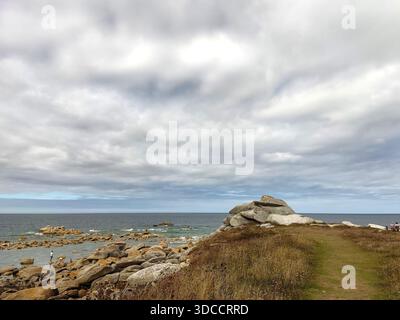 Plage de sable avec de grands rochers, mer calme et ciel nuageux. Une lumière douce et des textures naturelles créent une atmosphère côtière paisible. Banque D'Images