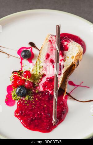 Tranche de cheesecake garnie de baies fraîches et de sauce vibrante Banque D'Images