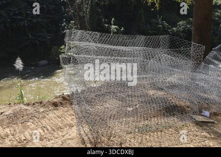 Paniers empilés en maille de gabion argentée en attente sur sol sec pour le projet de mur de soutènement de construction lourde montrant la préparation industrielle inachevée Banque D'Images