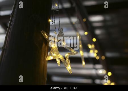 Lumière de fée en forme d'étoile illuminée suspendue sur un poteau en bois brille avec un sentiment chaleureux et festif contre le bokeh de fond flou foncé d'autres décorati Banque D'Images